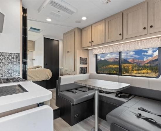 Im Road Bear RV Super Van Camper 23-25 stehen Sitzgruppe, Tisch und Küche neben dem Schlafzimmer und einem Panoramafenster.