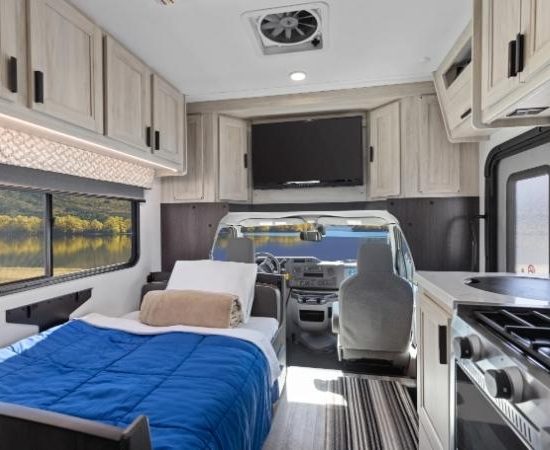 Im Road Bear Super Van Camper sind ein Bett, die Küchenzeile und das Fahrerhaus mit Blick nach vorn zu sehen.