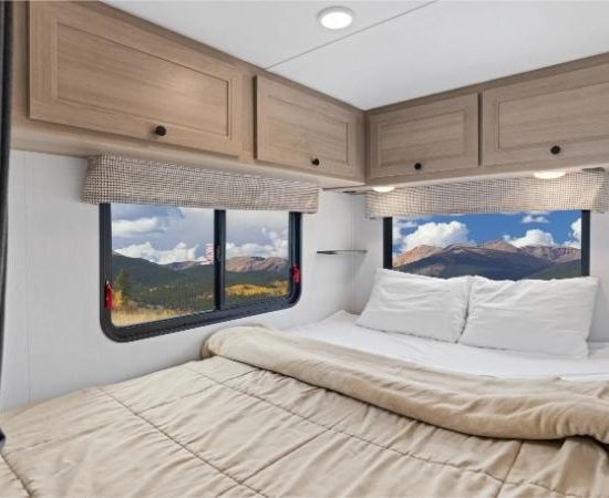 Im Schlafzimmer des Road Bear Super Van Camper stehen ein großes Bett und zwei Fenster mit Bergblick.