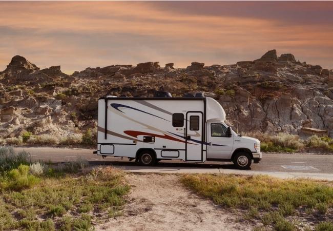 Ein weißer Road Bear Super Van Camper steht auf einer Straße vor felsiger Wüstenlandschaft im warmen Abendlicht.
