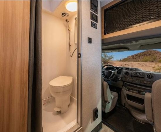 Ein Cruise America Wohnmobil zeigt links ein kompaktes Bad mit Toilette und rechts die Fahrerkabine.