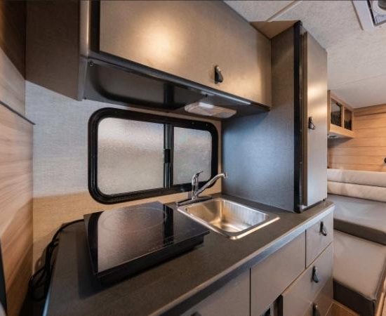 Im Cruise America C18 Ultra Compact stehen Spüle, Kochfeld und Schränke in einer kompakten Wohnmobilküche neben der Sitzbank.