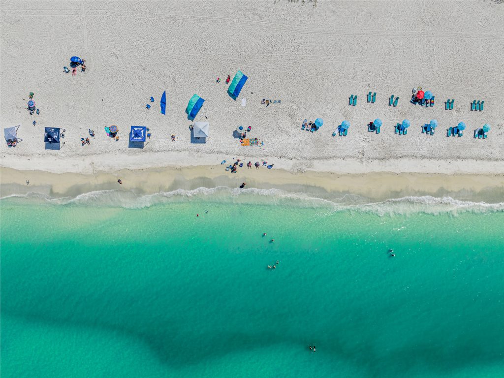 Türkisfarbenes Wasser und weißer Sandstrand von Holmes Beach auf Anna Maria Island mit Badegästen und Sonnenschirmen