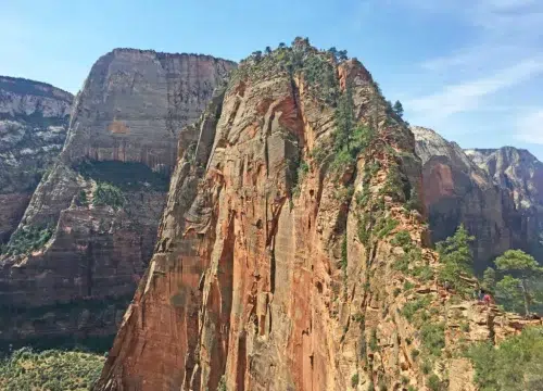 Die steilen, sandsteinfarbenen Felsen von Angels Landing ragen über dem Zion National Park in den blauen Himmel.