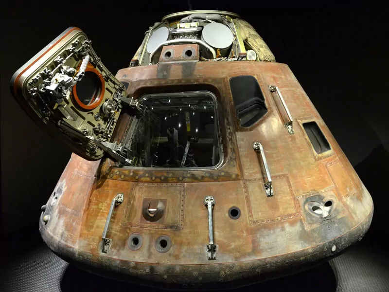 Im Kennedy Space Center steht eine originale Apollo-Raumkapsel mit geöffneter Luke und rostbrauner Außenhülle.