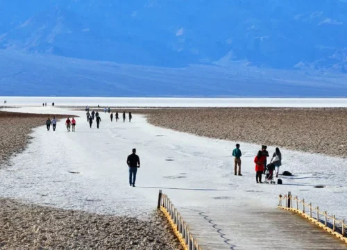 Besucher gehen über die helle Salzfläche von Badwater im Death Valley National Park, eingerahmt von Bergen.
