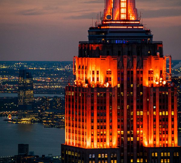 Das orange beleuchtete Empire State Building ragt bei Dämmerung über die nächtliche Skyline von New York hinaus.