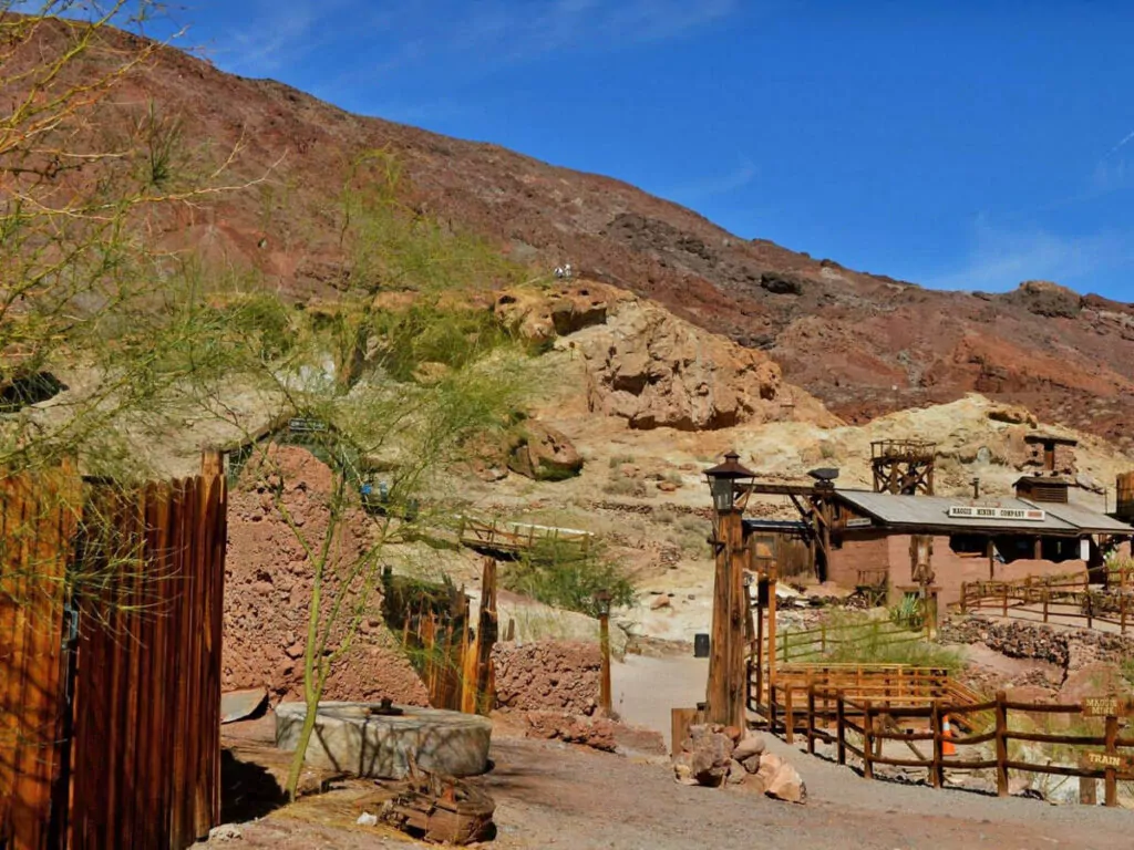 Historische Gebäude von Calico Ghost Town liegen vor rotbraunen Felsen und trockener Wüstenvegetation in Kalifornien.