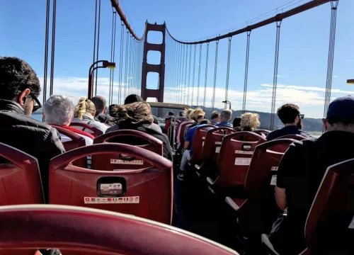 Passagiere sitzen im offenen Doppeldeckerbus und überqueren die rote Golden Gate Bridge in San Francisco.