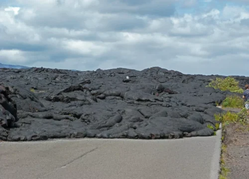 Eine breite Fläche aus schwarzer erkalteter Lava liegt am Hawaiian Volcanoes National Park unter bewölktem Himmel.