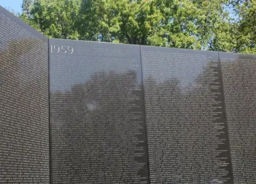 Dicht beschriftete Granitwand mit dem Jahr 1959 am Korean War Veterans Memorial in Washington unter grünen Bäumen