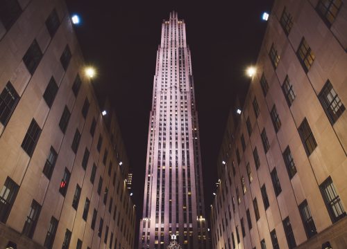 Nächtlicher Blick auf den beleuchteten Rockefeller-Center-Turm zwischen den Gebäudeflügeln in New York.