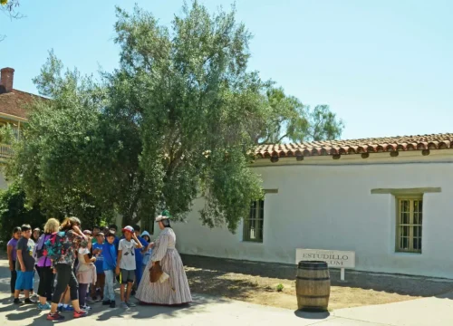 Besuchergruppe mit kostümierter Führerin vor einem historischen weißen Gebäude im Old Town San Diego, San Diego