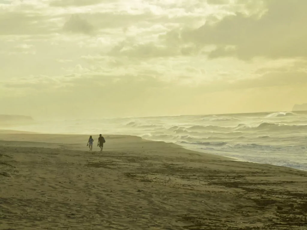 Zwei Menschen gehen am feinen Sandstrand des Polihale State Park auf Kauai bei Sonnenuntergang am Meer entlang.