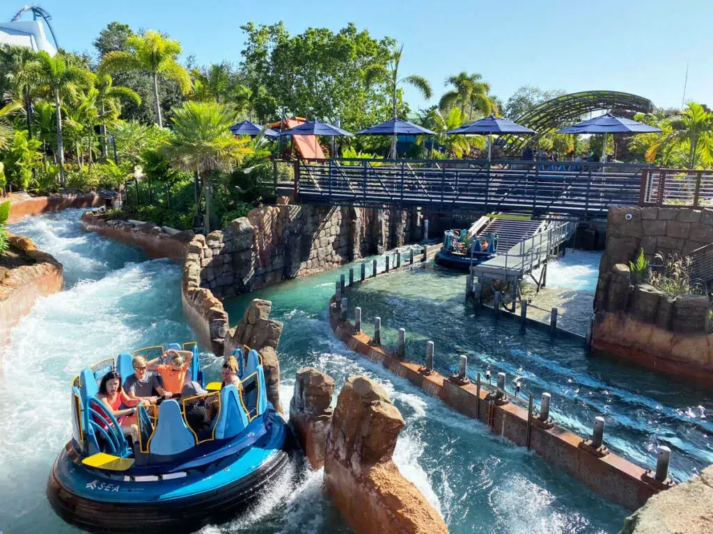 Ein blaues Rundboot fährt durch eine spritzende Wasserbahn unter Palmen im Freizeitpark SeaWorld Orlando in Florida.