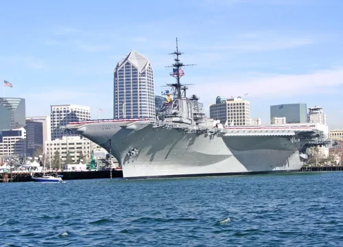 Vom Wasser aus ist der graue Flugzeugträger USS Midway vor der Skyline von San Diego im Hafen zu sehen.