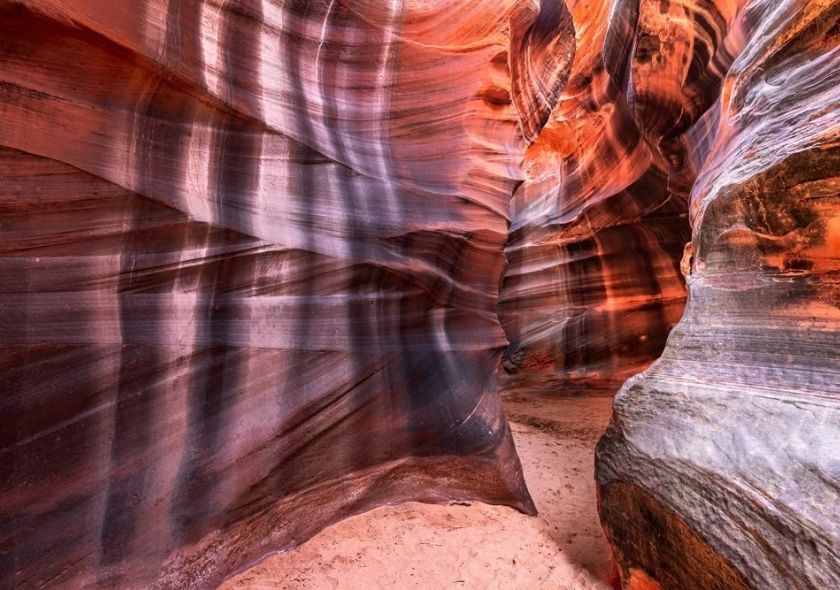 Im Antelope Canyon verlaufen geschwungene Sandsteinwände in Rot, Orange und Violett; schmale Lichtstrahlen fallen auf den Canyonboden.