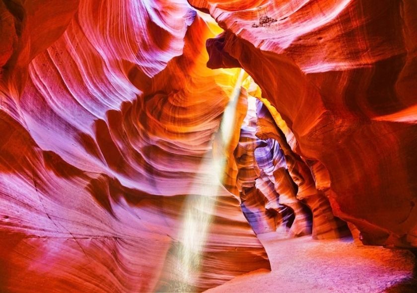 Ein schmaler Lichtstrahl fällt zwischen den geschwungenen roten Sandsteinwänden des Upper Antelope Canyon bis auf den Canyonboden.